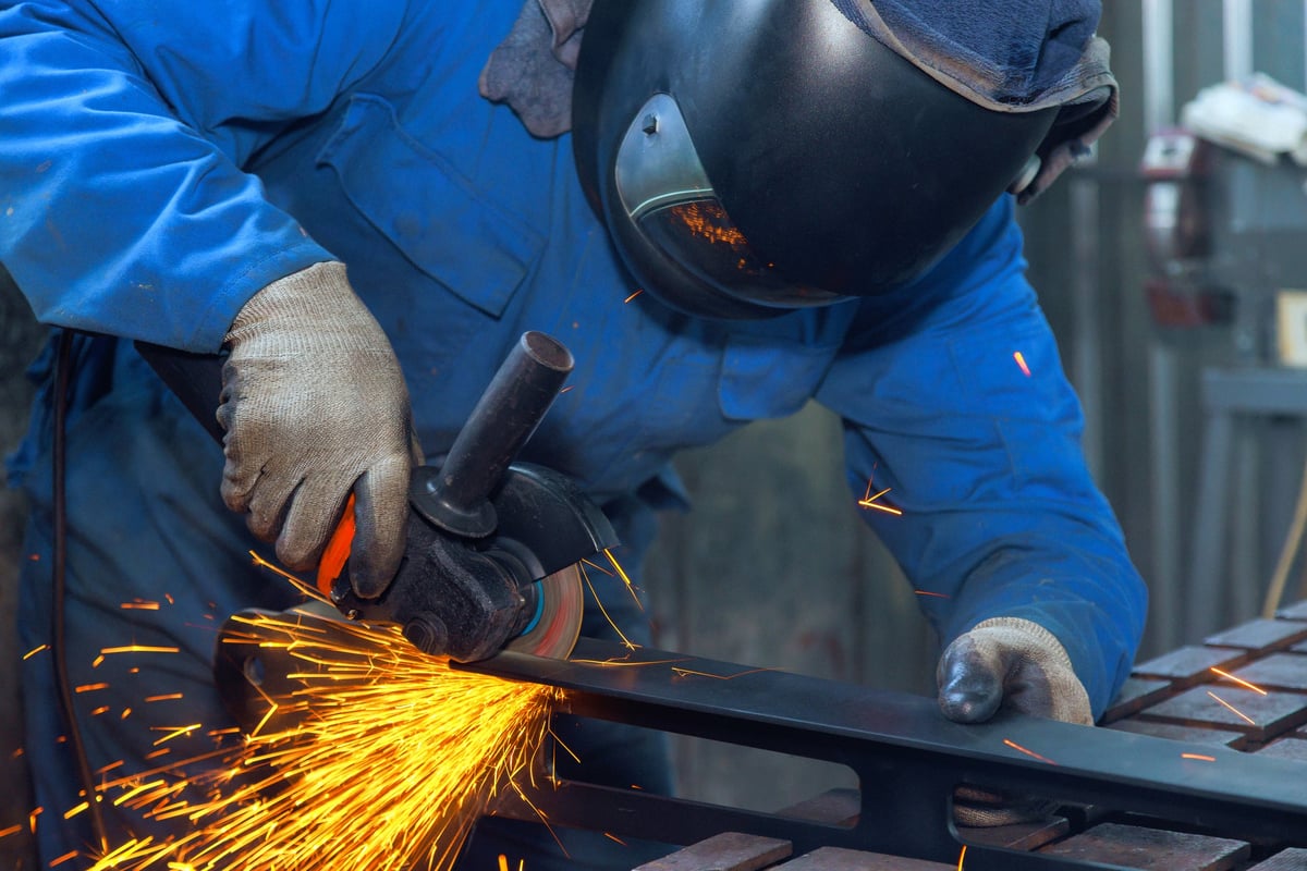 Worker in safety gear grinds metal, creating sparks, showcasing craftsmanship at metal workshop