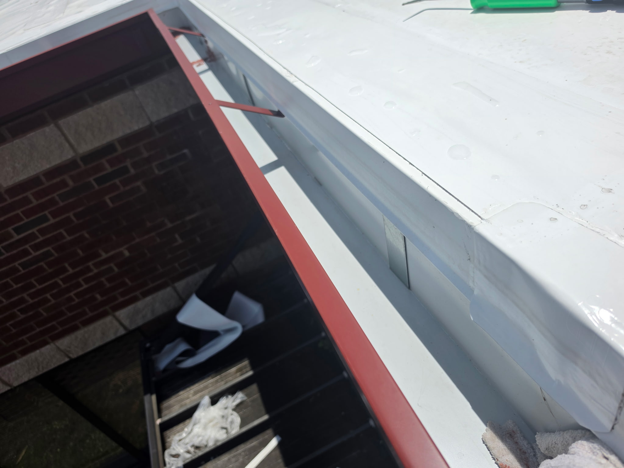 Close-up of MPI's GT-1 aluminum box gutter installed on the New Midway Middle School roof, showing white metal profile against the brick parapet and red steel structural framing